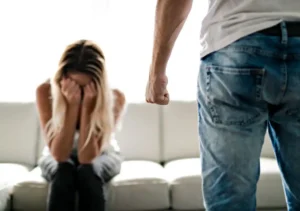 woman crying on couch while angry man stands nearby with fist