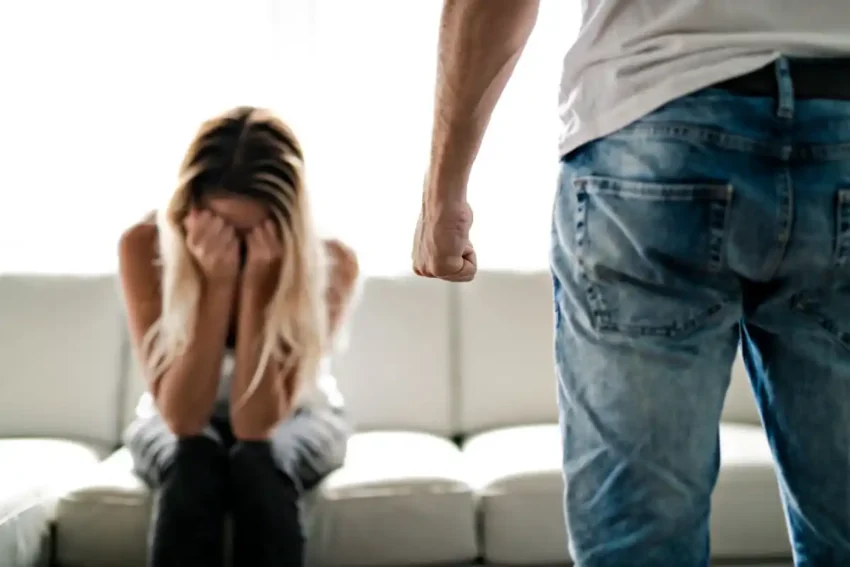 woman crying on couch while angry man stands nearby with fist