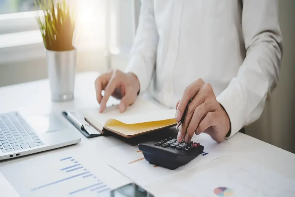 person calculating finances at desk with documents laptop and calculator
