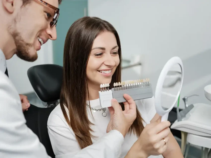dentist comparing tooth shades with smiling patient using mirror